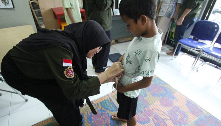 Seorang anggota Karang Taruna sedang mengukur lingkar pinggang seorang anak